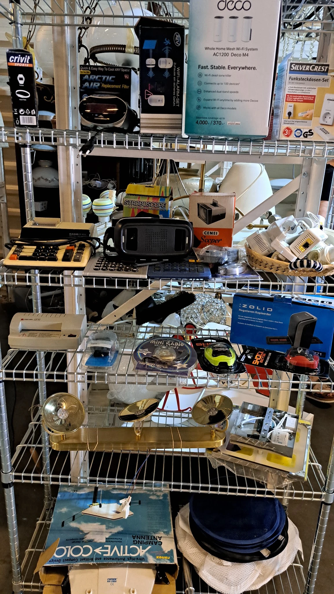 Diverse tweedehands spullen op stellingen: elektronika, speelgoed, huishoudartikelen en andere goederen