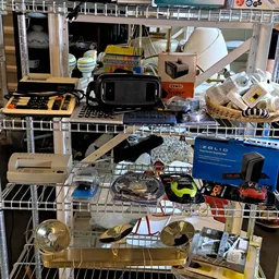 Diverse tweedehands spullen op stellingen: elektronika, speelgoed, huishoudartikelen en andere goederen