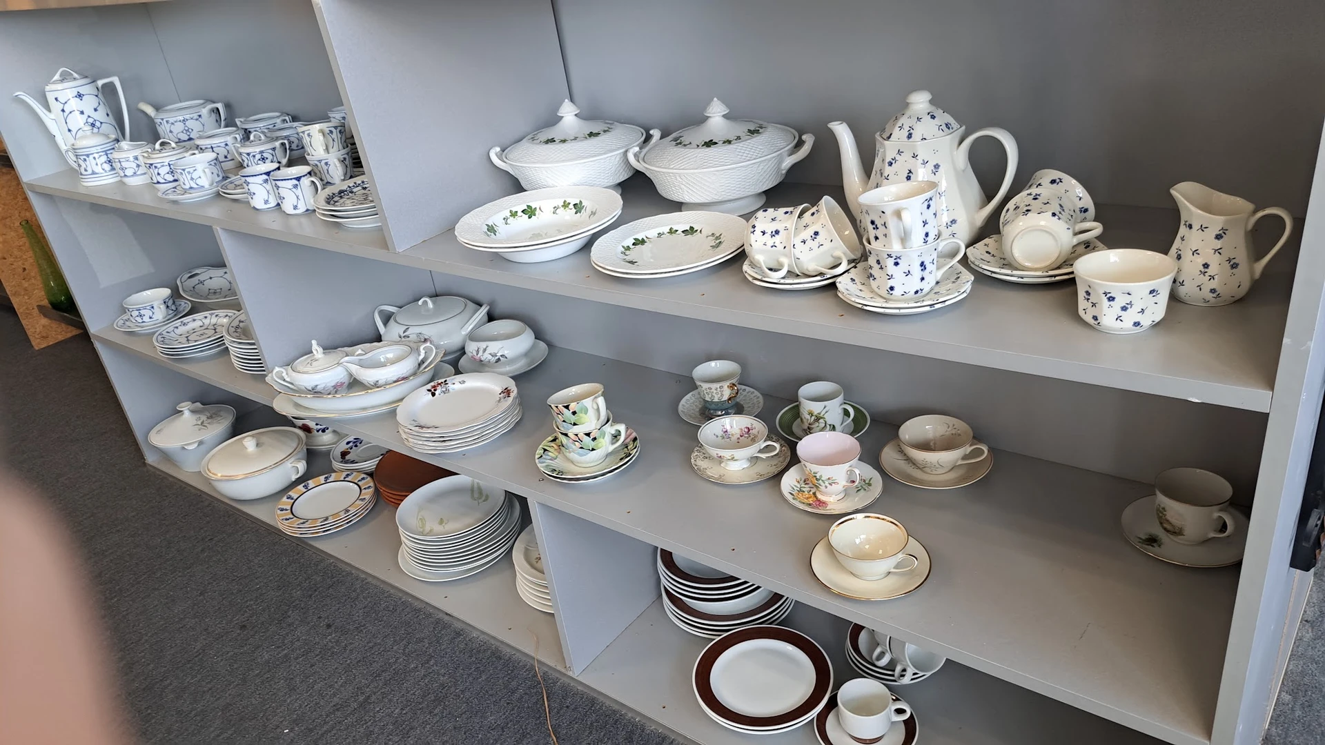 Stellingen met serviesgoed: kommen, borden, kopjes, kannen en schalen in wit en blauw porselein