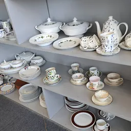 Stellingen met serviesgoed: kommen, borden, kopjes, kannen en schalen in wit en blauw porselein