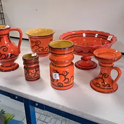 Uitgestalde rode en oranje serviesgoed met decoratieve patronen op een witte tafel
