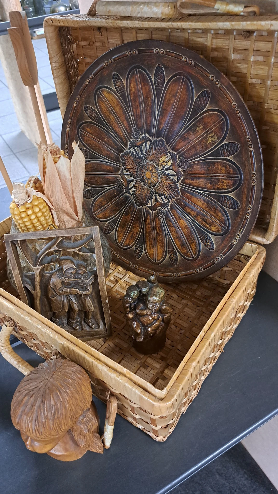 Houten mandje met diverse houten en bronzen decoratieve items, waaronder een bloemmotief, maïskolf, en beelden