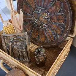 Houten mandje met diverse houten en bronzen decoratieve items, waaronder een bloemmotief, maïskolf, en beelden