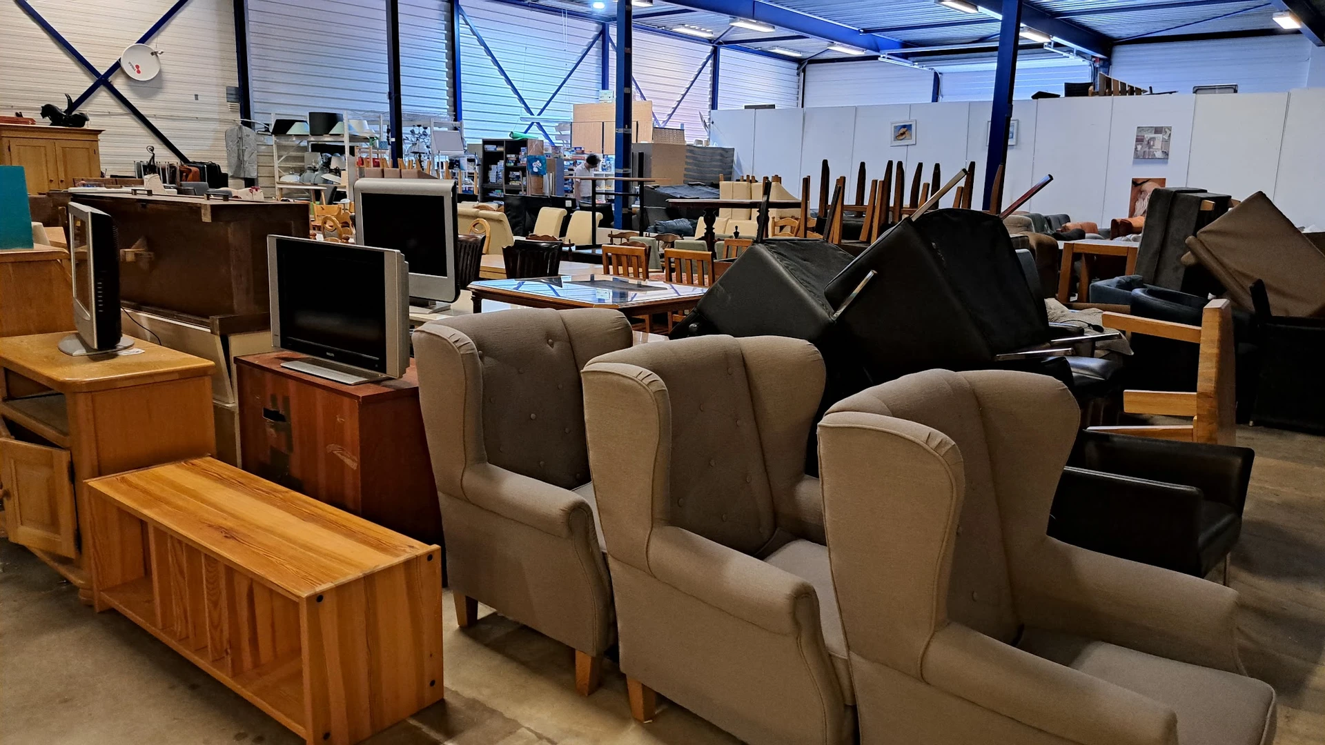 Beige en grijze fauteuils in een kringloopwinkel met op de achtergrond meer meubels en huishoudelijke spullen
