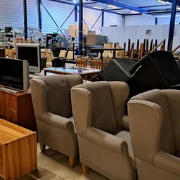 Beige en grijze fauteuils in een kringloopwinkel met op de achtergrond meer meubels en huishoudelijke spullen