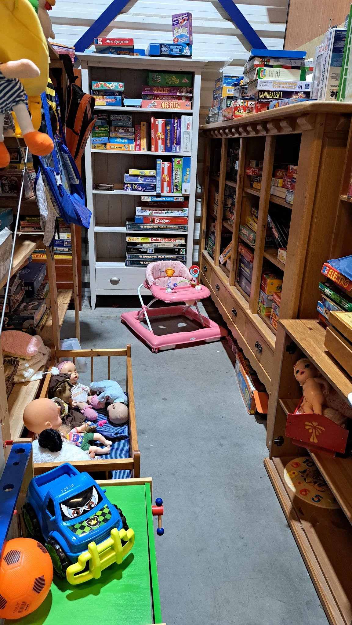 Winkelinterieur met houten stellingen vol spullen, roze babywalker en kinderspeelgoed op betonnen vloer