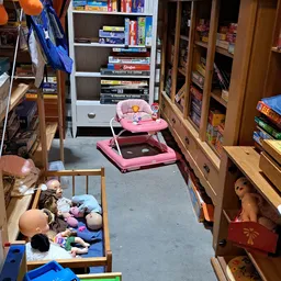 Winkelinterieur met houten stellingen vol spullen, roze babywalker en kinderspeelgoed op betonnen vloer
