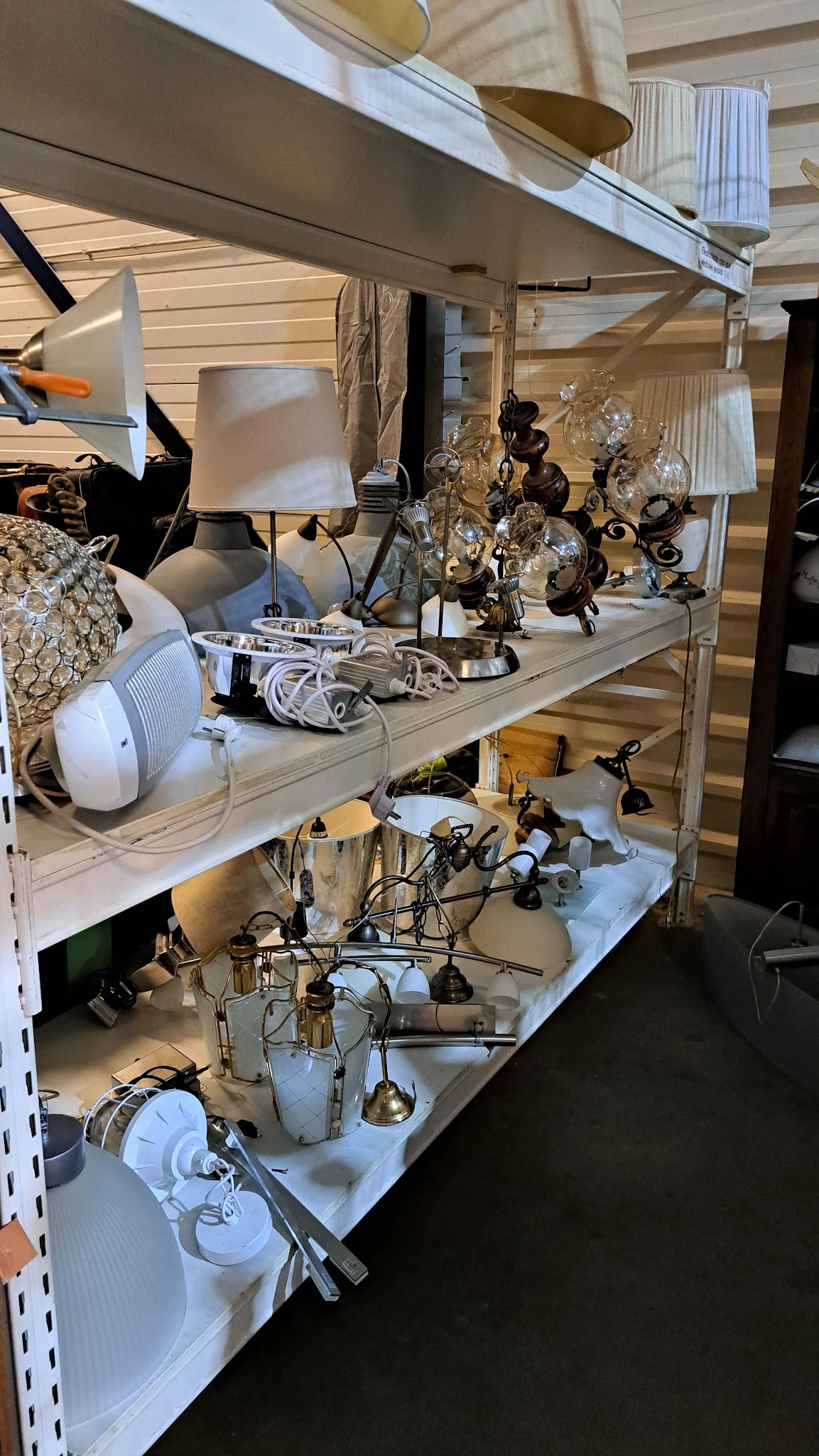 Twee stellingen met diverse tweedehands lampen en verlichtingsartikelen met witte kabels