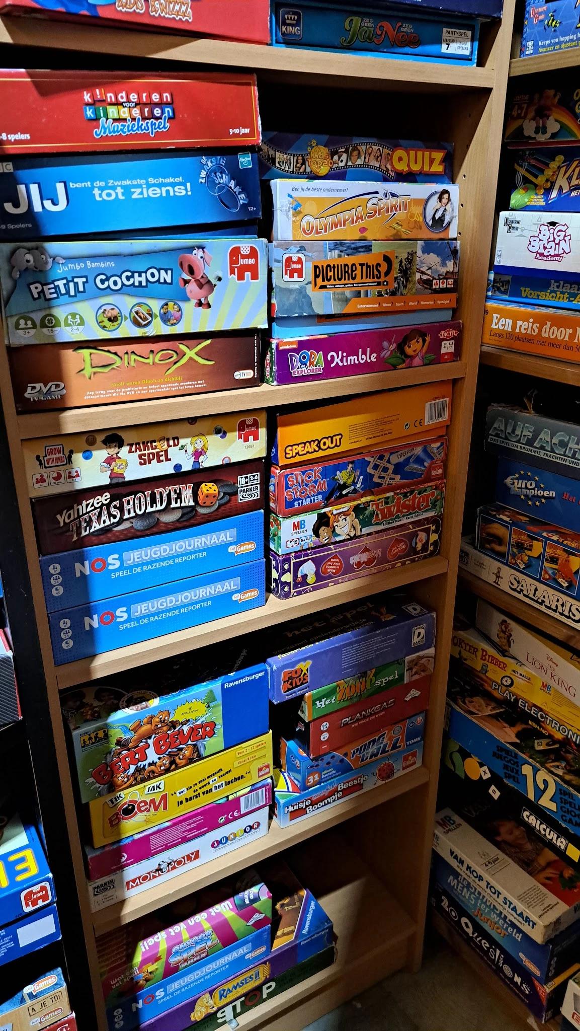 Houten stellingen vol met bordspellen en DVD's, waaronder titels als Dimble, Yahtzee en Speak Out