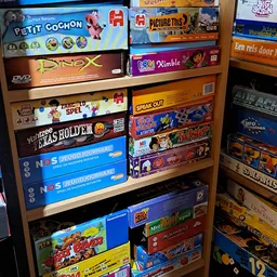 Houten stellingen vol met bordspellen en DVD's, waaronder titels als Dimble, Yahtzee en Speak Out