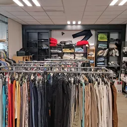 Rekken met tweedehands kleding in diverse kleuren, op de achtergrond stellingen met dozen en tassen
