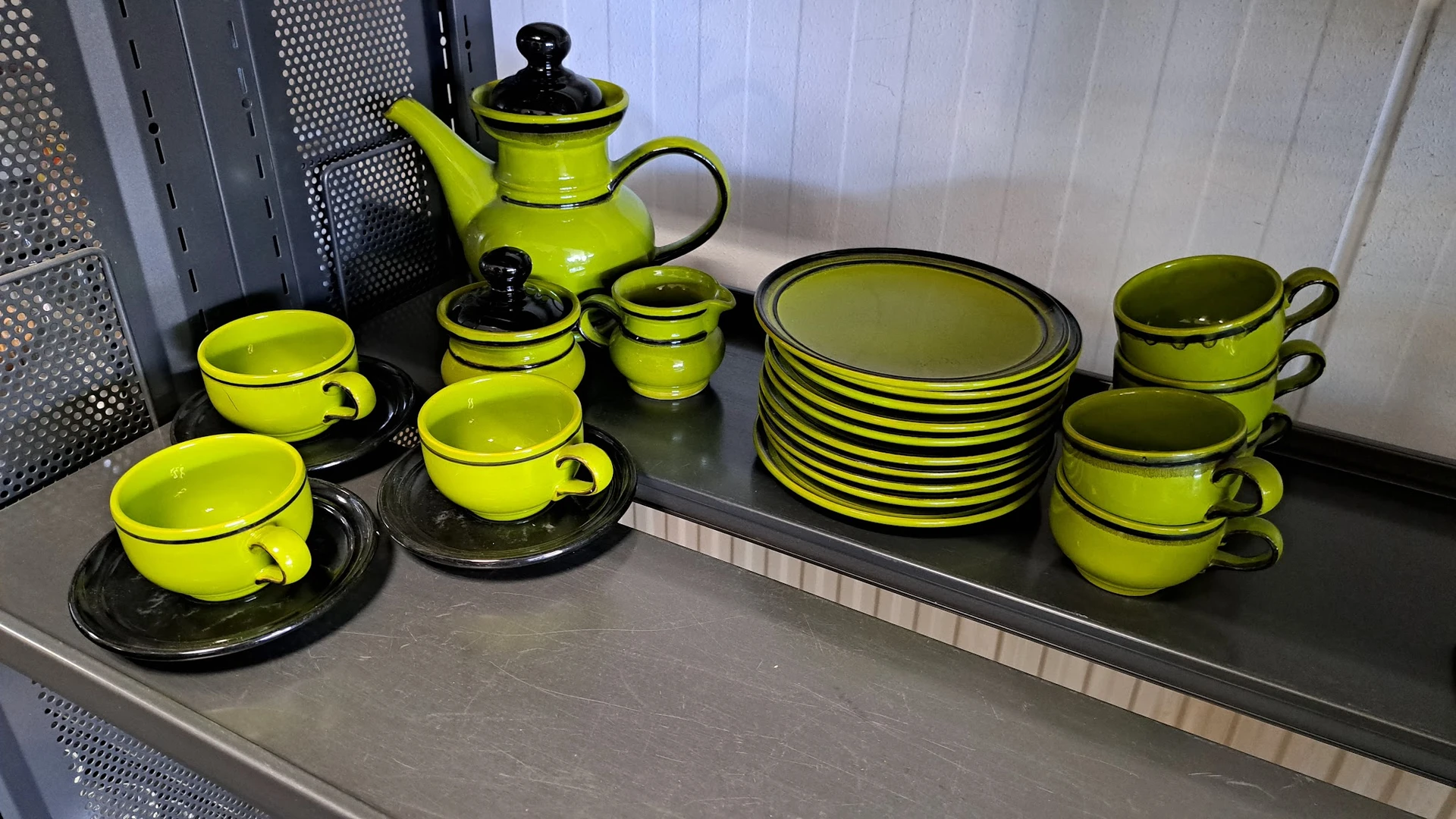 Geel en zwart servies met theepot, kopjes, schotels en borden op een donker oppervlak.