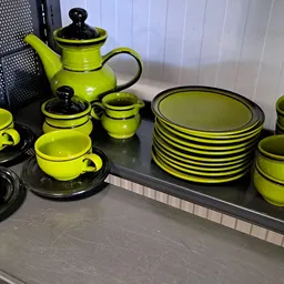Geel en zwart servies met theepot, kopjes, schotels en borden op een donker oppervlak.