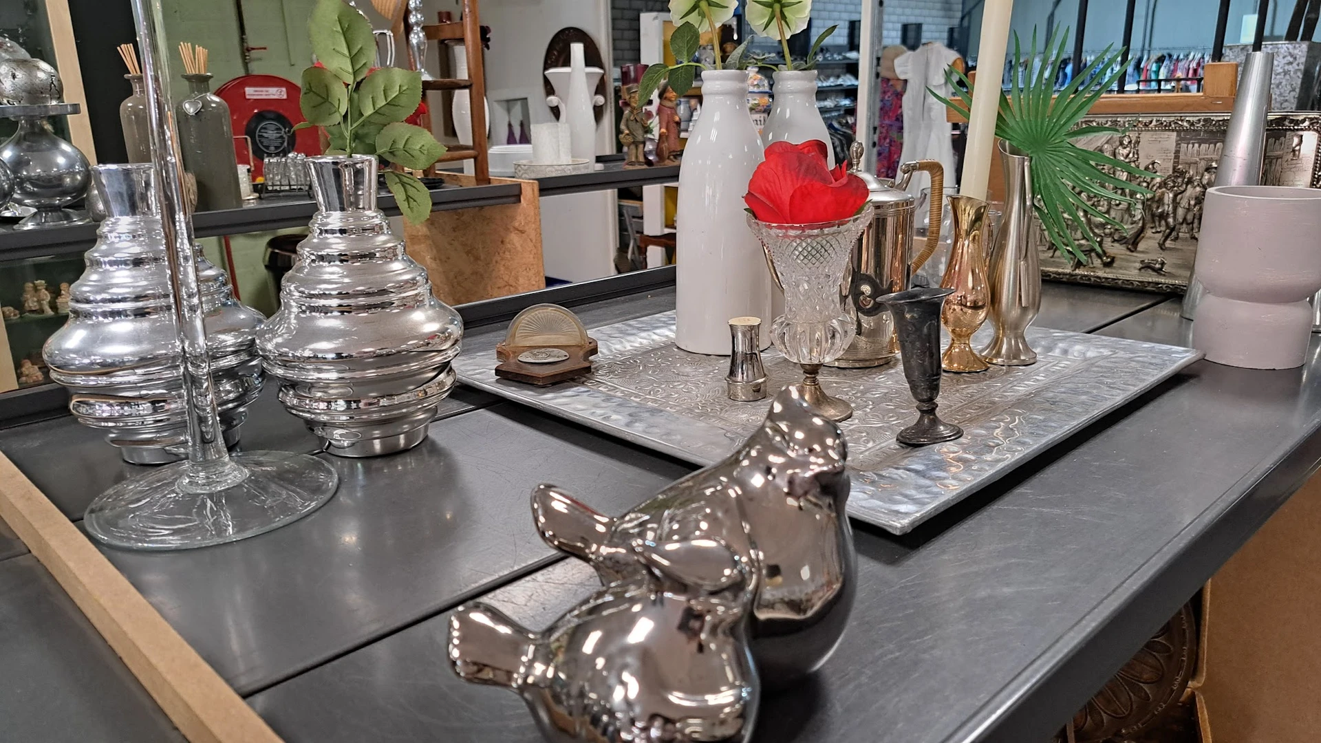 Vitrinekast met diverse decoratieve items: glazen vazen, zilveren beeldjes, vazen en rode stoffering