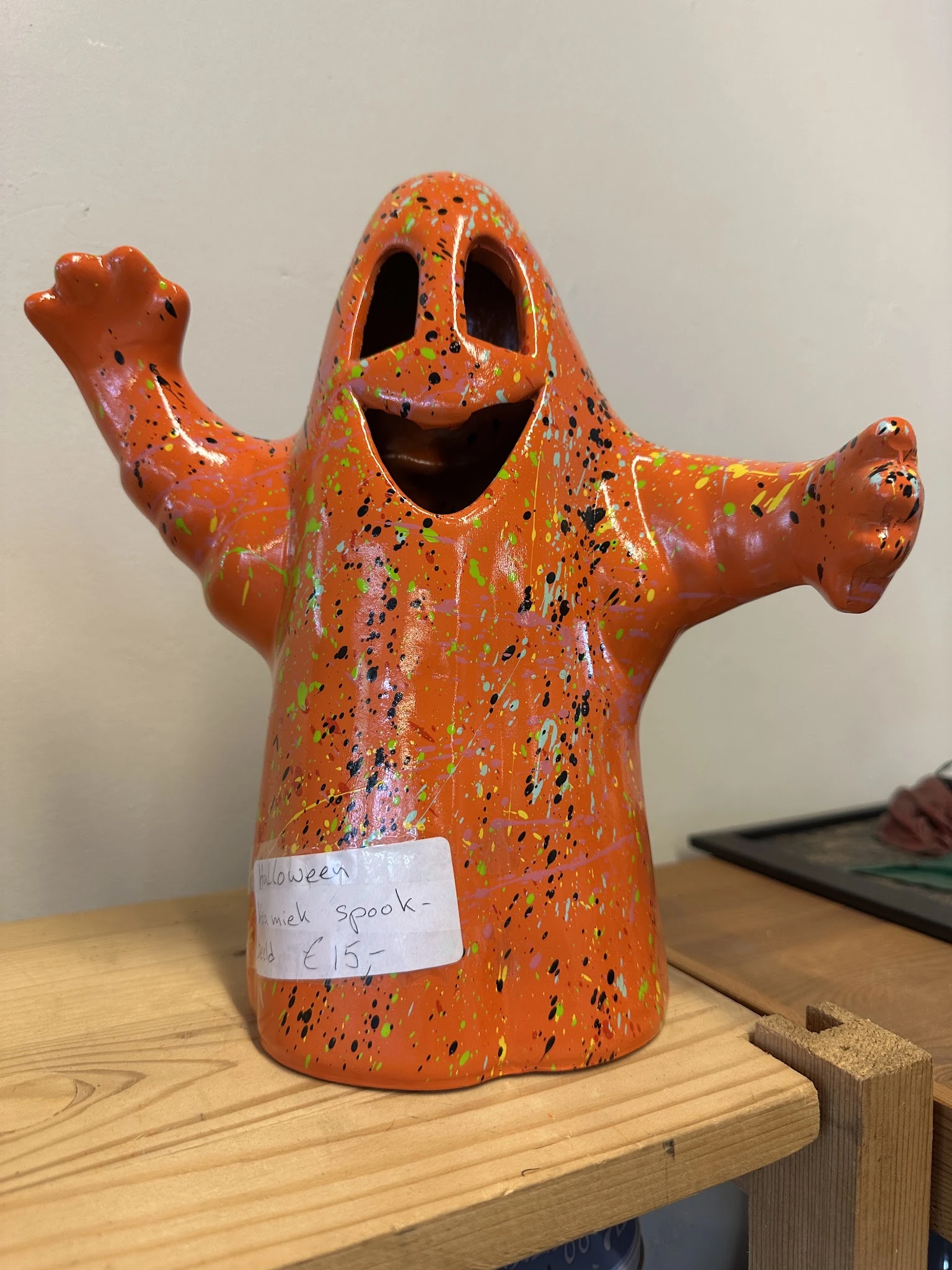 Oranje keramische spookfiguur met zwarte stippen en een prijskaartje, armen uitgestrekt