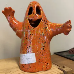 Oranje keramische spookfiguur met zwarte stippen en een prijskaartje, armen uitgestrekt