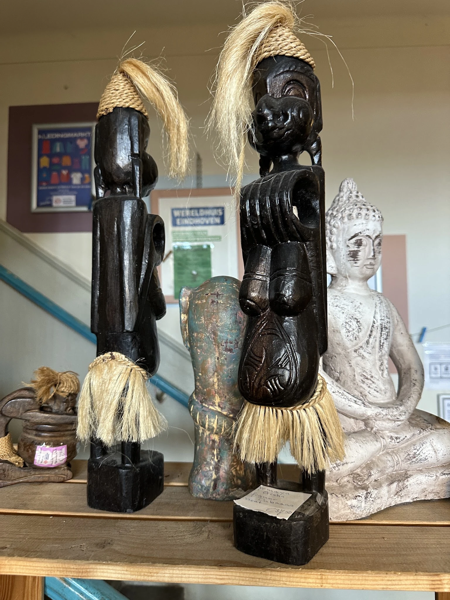 Beeldhouwwerk en decoratieve items uitgestald: zwarte houten beelden met raffia, een gepatineerde bronzen vaas en een witte b