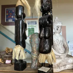 Beeldhouwwerk en decoratieve items uitgestald: zwarte houten beelden met raffia, een gepatineerde bronzen vaas en een witte b