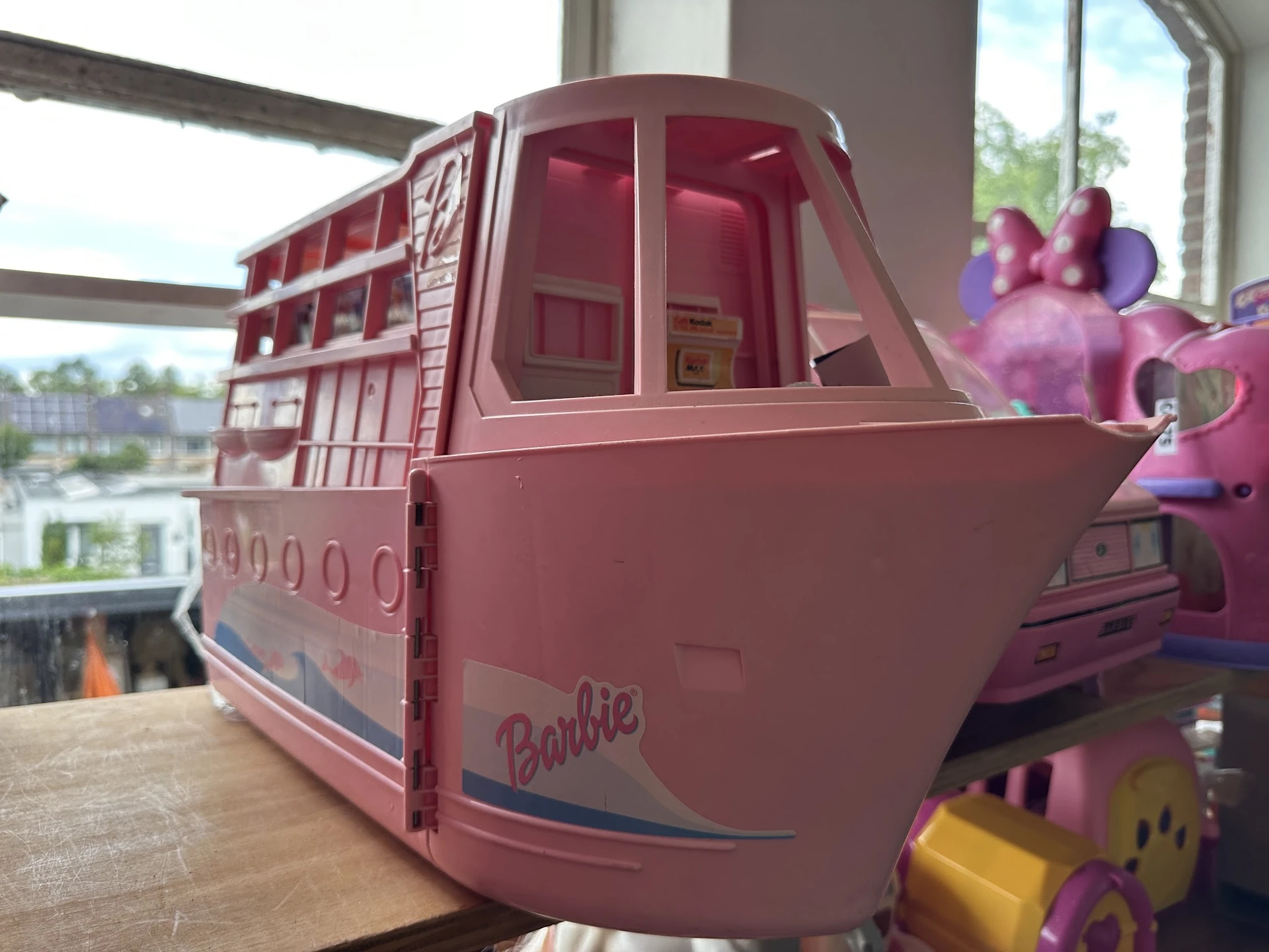 Roze Barbie-speelgoedbus op houten tafel bij raam met uitzicht op water