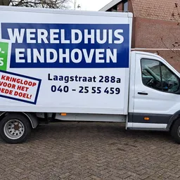 Witte bedrijfsbus met blauwe opdruk 'Wereldhuis Eindhoven' en contactgegevens op straat geparkeerd