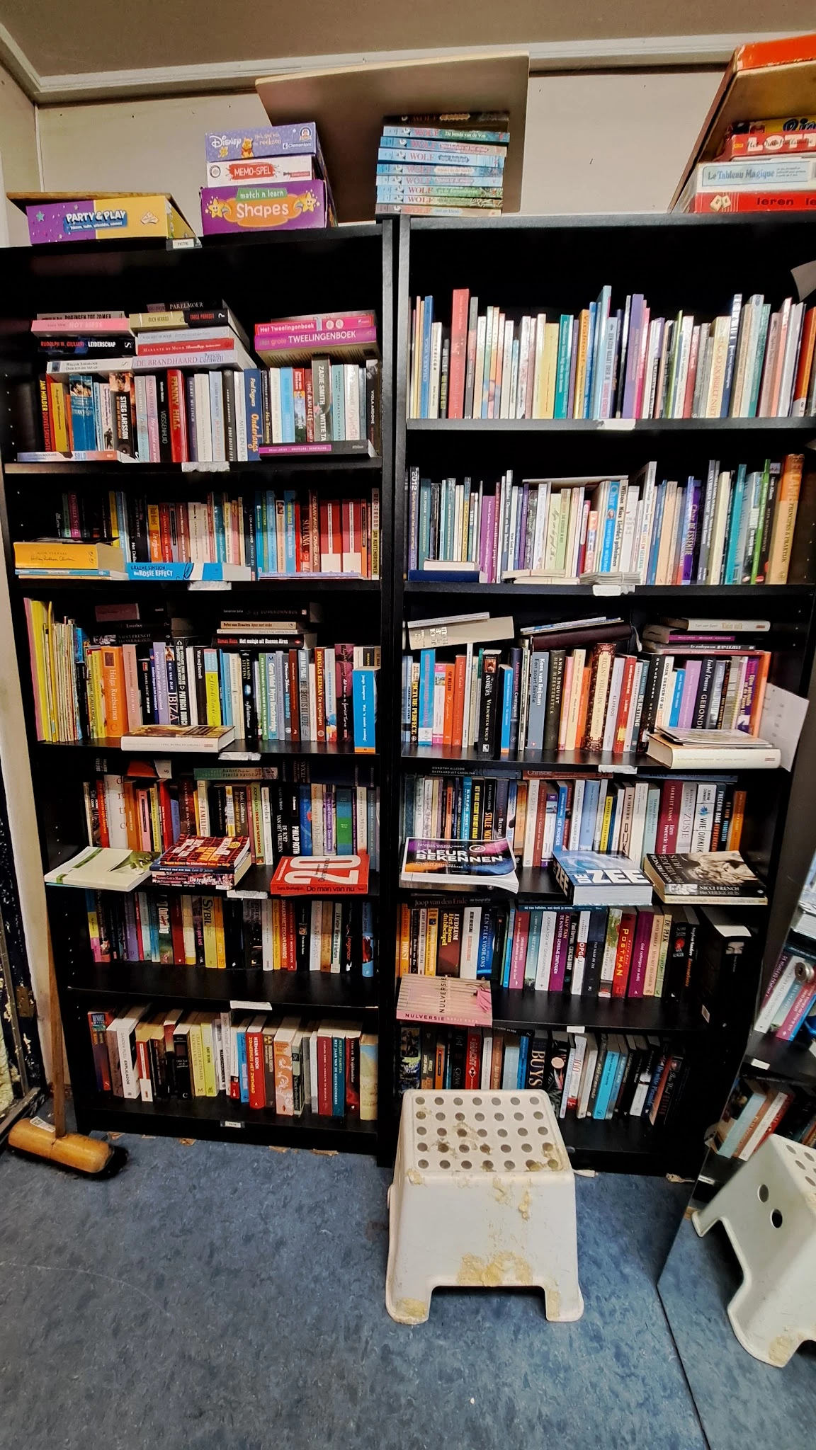 Zwarte boekenkast met veel tweedehands boeken en dvd's netjes uitgestald op meerdere niveaus