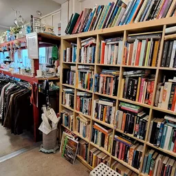 Grote boekenkast met honderden tweedehands boeken in verschillende kleuren, links ervan kleding op hangers