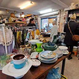 Winkelbinnenkant met tafels vol servies, kleding aan rekken, klanten aan het winkelen, volle schappen tegen muren