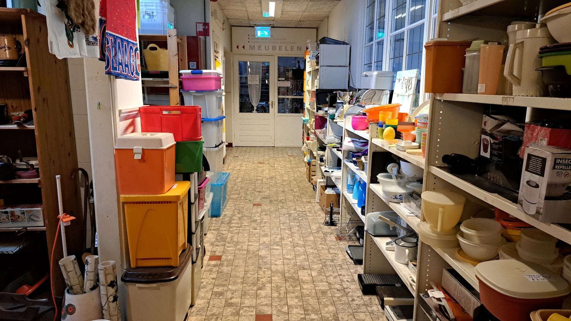 Winkelgang met stellingen vol serviesgoed, dozen en huishoudelijke artikelen