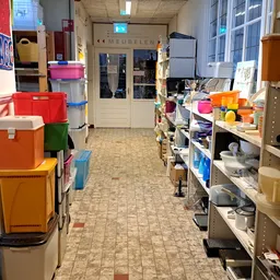 Winkelgang met stellingen vol serviesgoed, dozen en huishoudelijke artikelen
