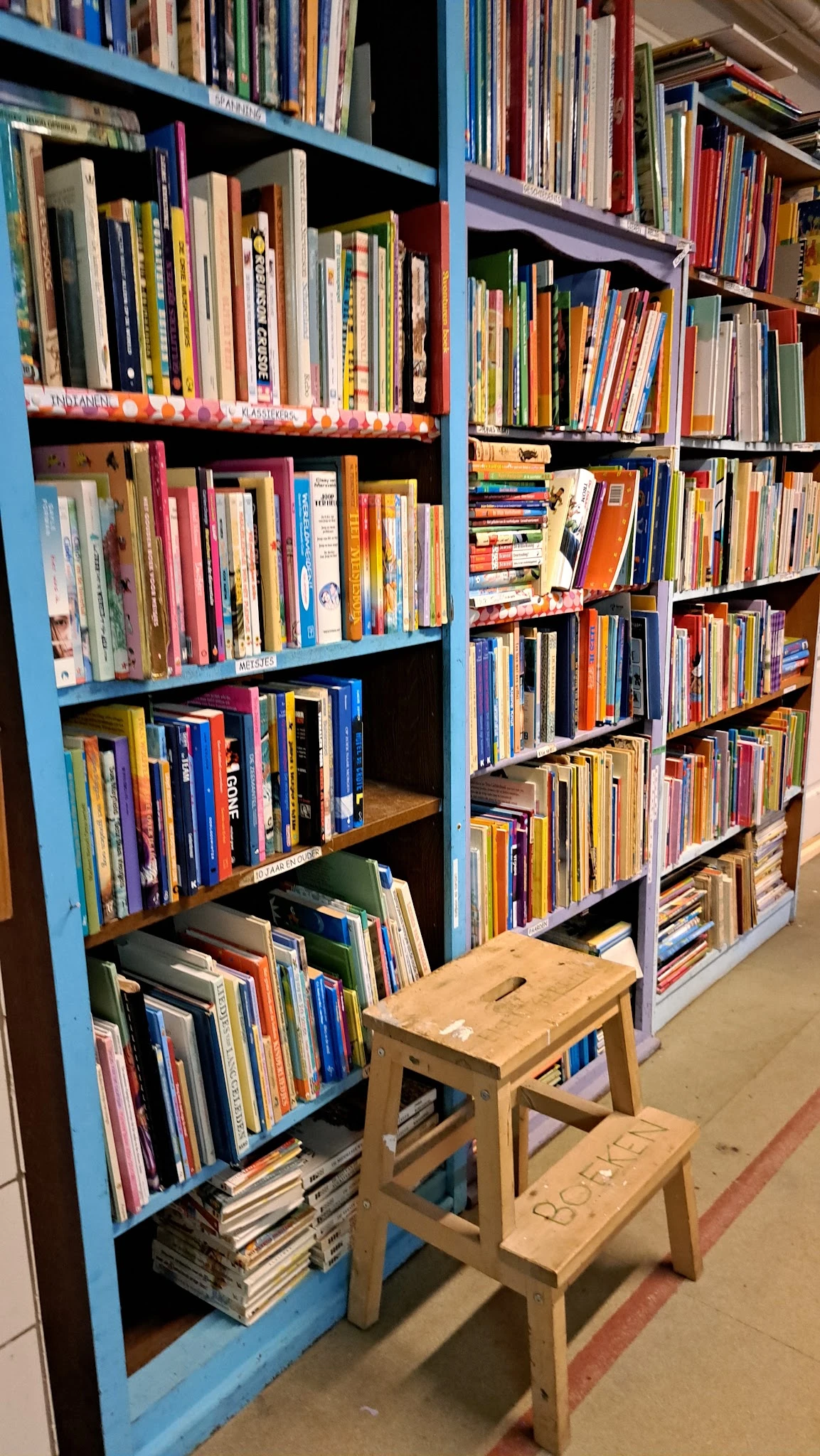 Boekenkast met veel tweedehands boeken en dvd's netjes uitgestald op verschillende planken