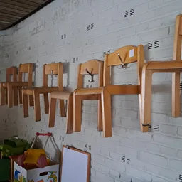 Houten stoelen en tafels opgehangen aan een witte bakstenen wand