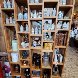 Houten wandkast met vakken vol decoratieve items: miniatuurschilderijtjes van huizen, porseleinen beeldjes, zwarte kettels, k