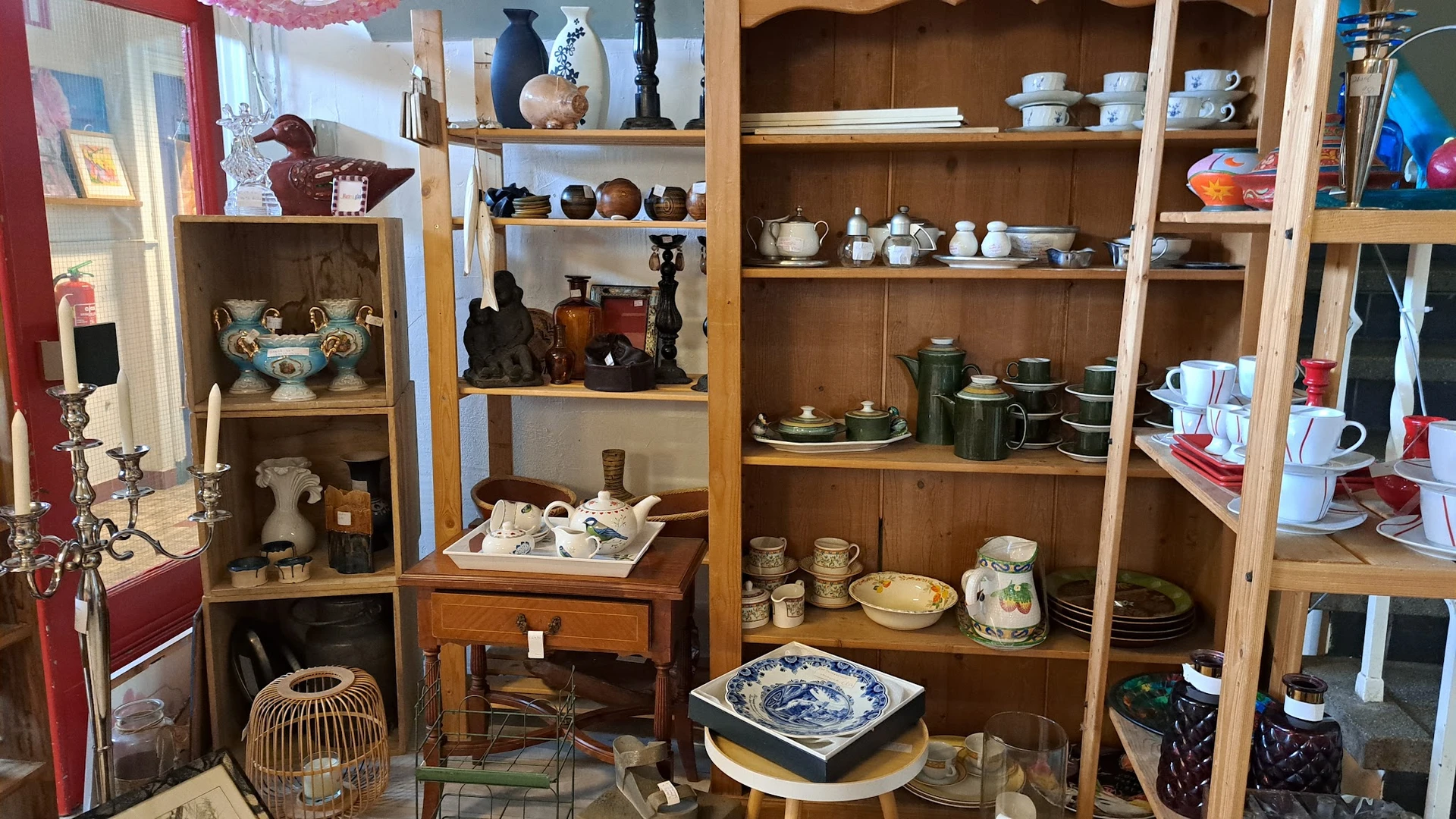 Houten kasten met diverse servies, vazen, beeldjes en huishoudelijke artikelen uitgestald