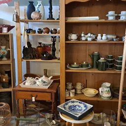 Houten kasten met diverse servies, vazen, beeldjes en huishoudelijke artikelen uitgestald
