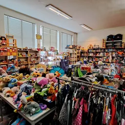 Winkelinterieur met speelgoed, kleding en boeken; tafels vol knuffels en pluche dieren, rek met kinderkleding, boekenkasten o