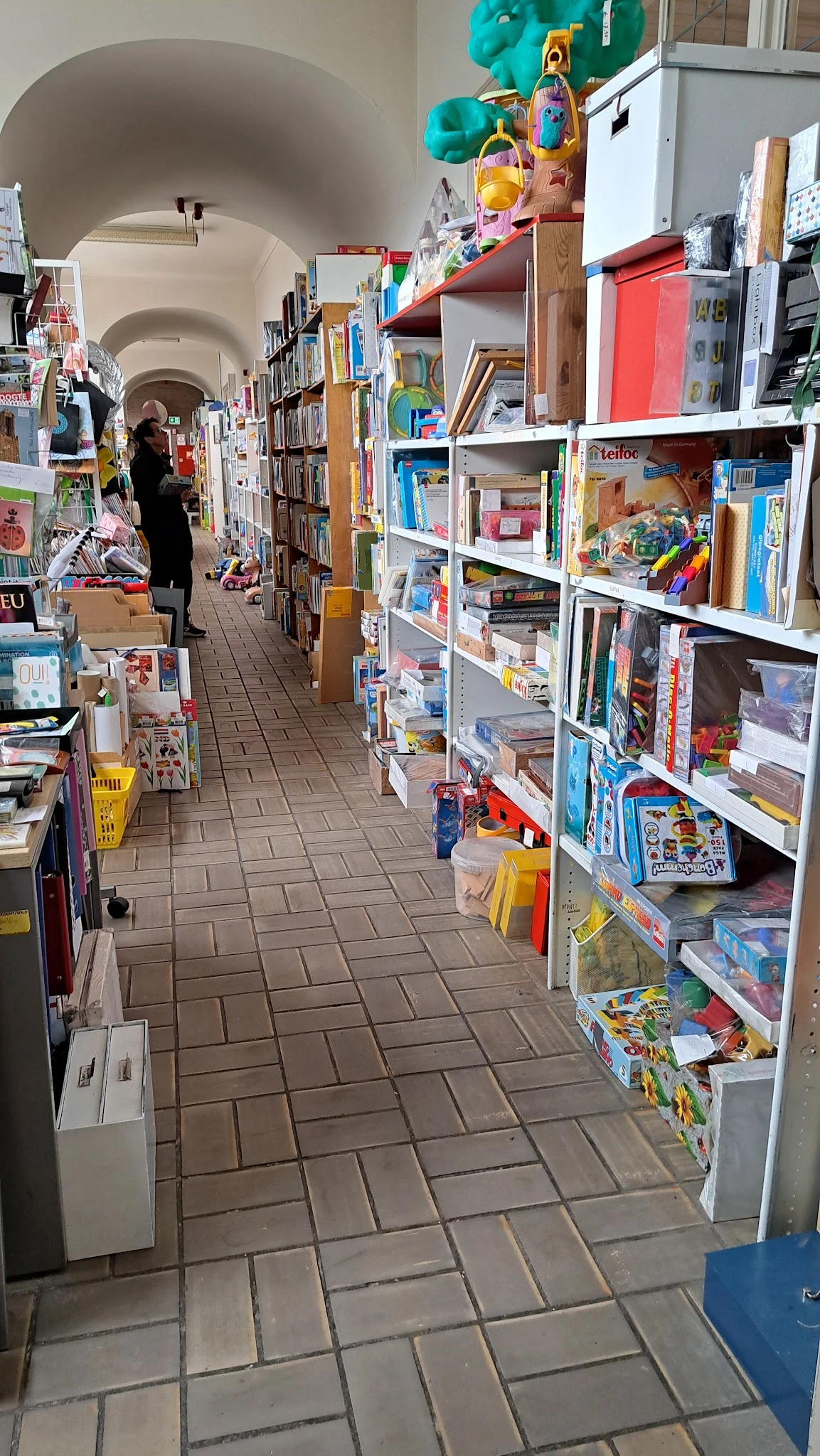 Winkelgangetje met witte stellingen vol boeken, speelgoed en huishoudartikelen aan beide zijden