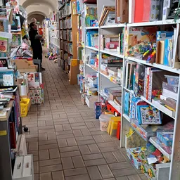 Winkelgangetje met witte stellingen vol boeken, speelgoed en huishoudartikelen aan beide zijden
