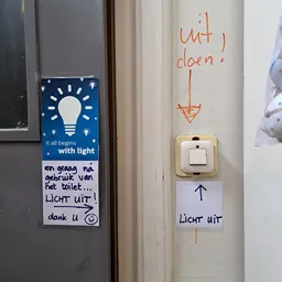 Lichtschakelaar met handgeschreven Nederlands en Engels tekstjes erop geplakt