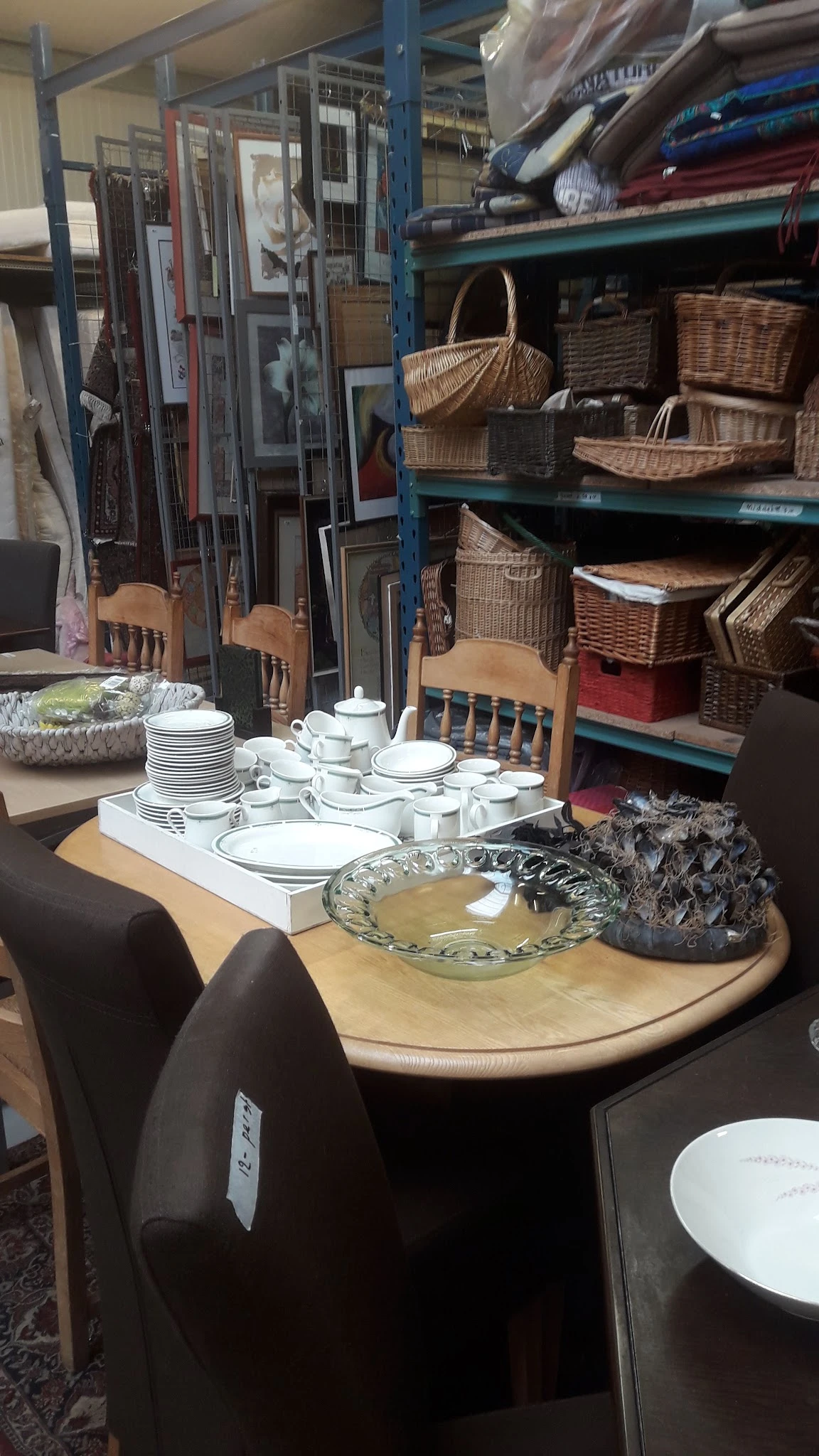 Displaytafel met servies, borden, kopjes en decoratieve items in een kringloopwinkel
