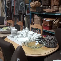 Displaytafel met servies, borden, kopjes en decoratieve items in een kringloopwinkel