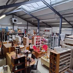 Overzicht van de winkelvloer met diverse meubels, stellingen en uitgestalde spullen in een ruime kringloopwinkel