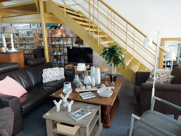 Woonkamer inrichting met zwarte leren banken, houten tafels en trap in de achtergrond