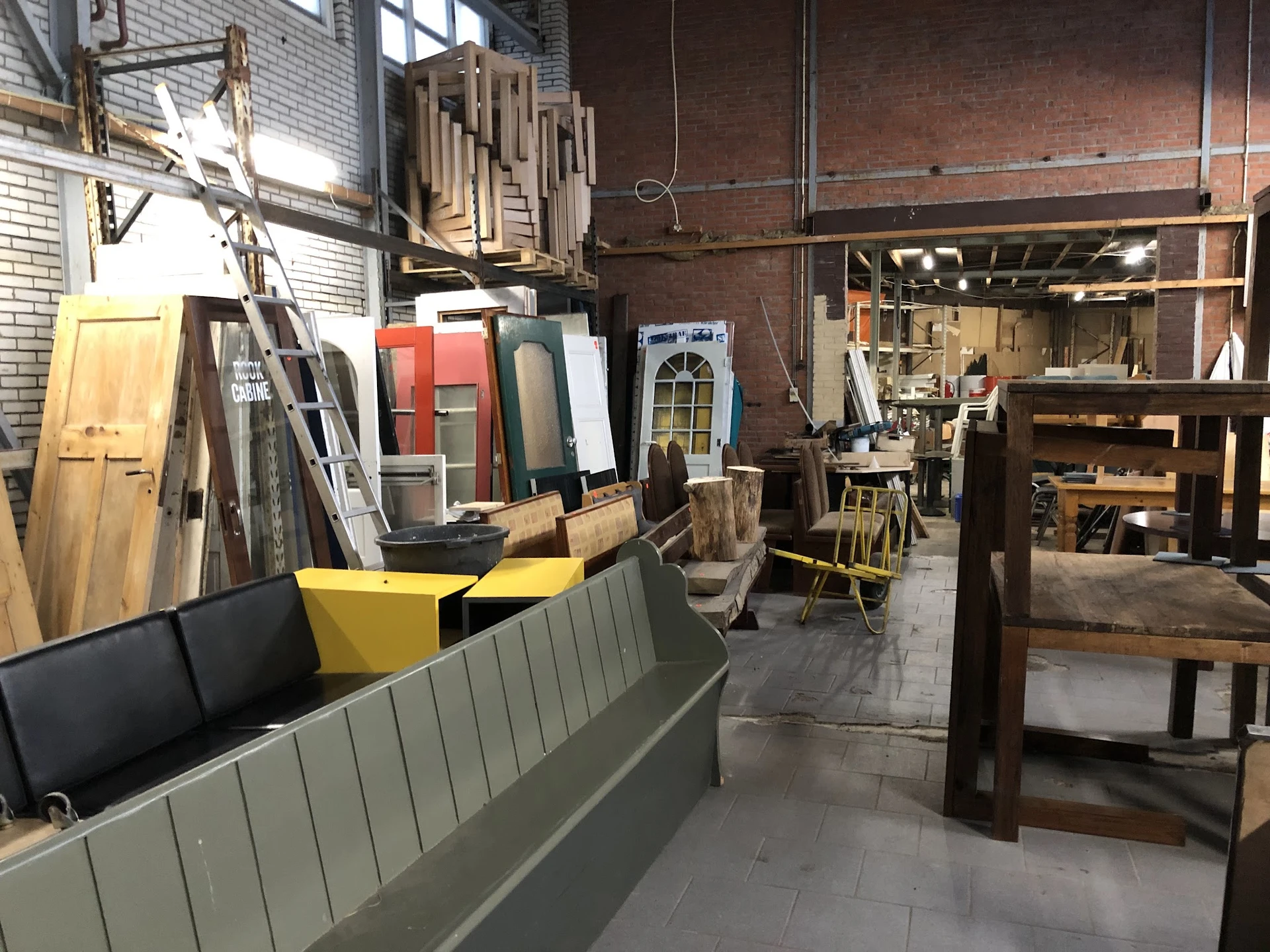 Winkelvloer met houten meubels, deuren, stellingen en diversen spullen in een ruime kringloopwinkel