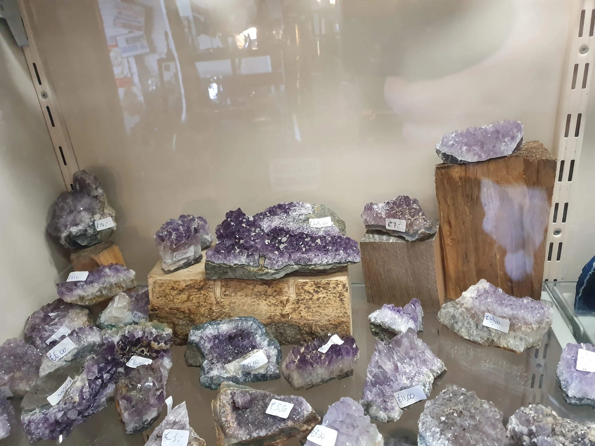Uitgestalde amethist kristalclusters en geodes op houten blokken en in rekken