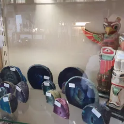 Glazen vitrinekast met verschillende blauwe helmen en decoratieve maskers op de achtergrond