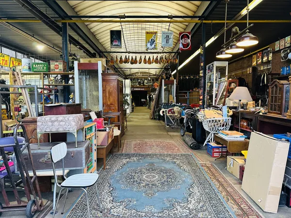 Binnenzicht van kringloopwinkel met diverse meubels, huishoudartikelen en spullen langs de wanden en in het gangetje