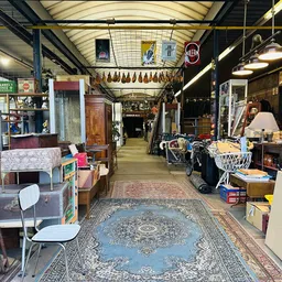 Binnenzicht van kringloopwinkel met diverse meubels, huishoudartikelen en spullen langs de wanden en in het gangetje