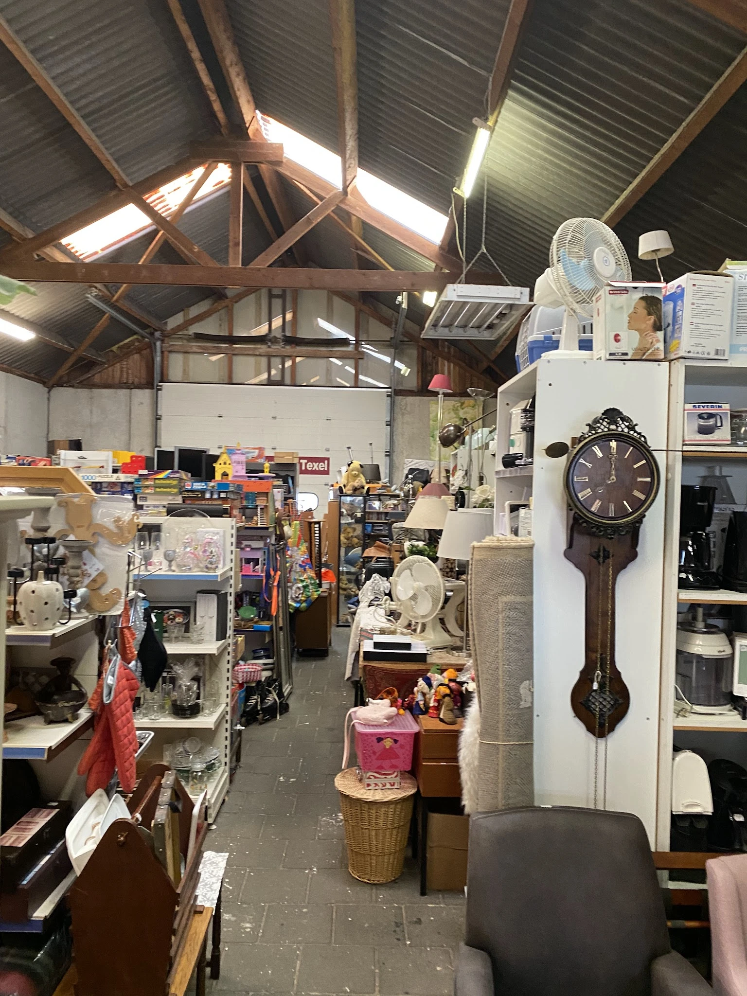 Binnenaanzicht van kringloopwinkel met stellingen, huishoudelijke artikelen, klokken en diverse gebruikte spullen