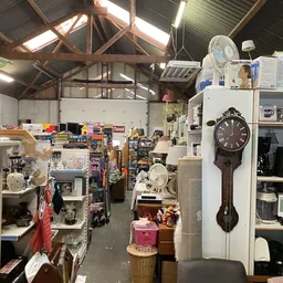 Binnenaanzicht van kringloopwinkel met stellingen, huishoudelijke artikelen, klokken en diverse gebruikte spullen