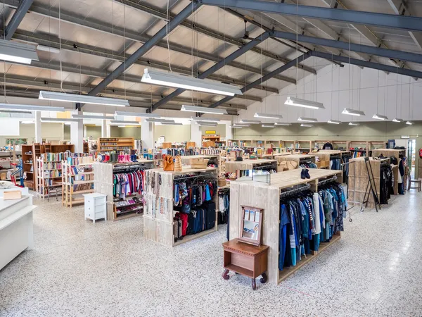 Ruim winkelvloer met kledingrekken, stellingen en winkelafdelingen in een kringloopwinkel